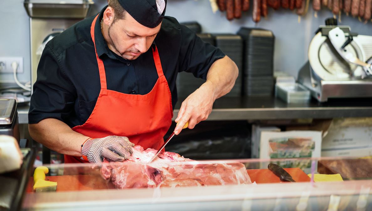 Boucher Avec Son Tablier Et Ses Gants Qui Découpe De La Viande Dans Son Magasin